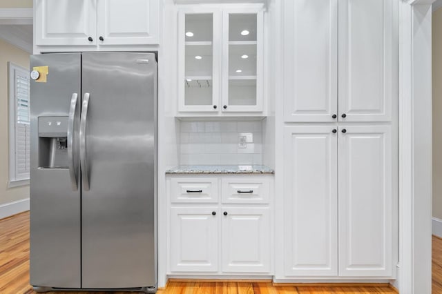 kitchen with white cabinets, light hardwood / wood-style floors, backsplash, stainless steel fridge with ice dispenser, and light stone counters