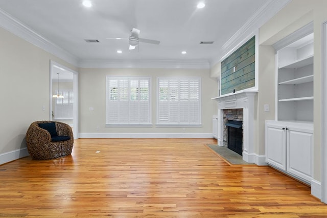 living room featuring built in features, light hardwood / wood-style flooring, crown molding, and a stone fireplace