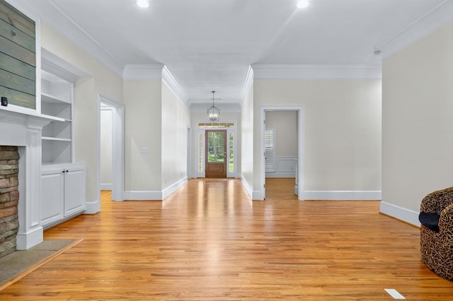 unfurnished living room featuring a stone fireplace, crown molding, built in shelves, light hardwood / wood-style flooring, and an inviting chandelier