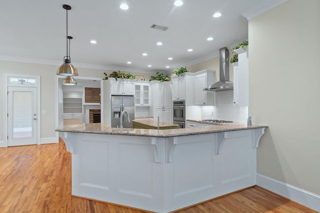 kitchen with kitchen peninsula, white cabinetry, wall chimney range hood, and stainless steel appliances