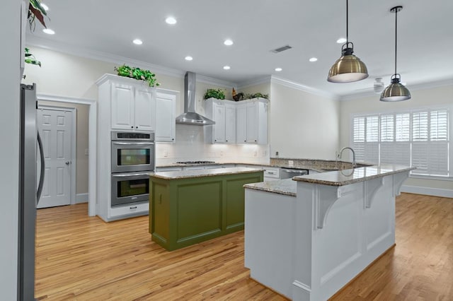 kitchen with appliances with stainless steel finishes, wall chimney exhaust hood, a kitchen island, white cabinetry, and light stone counters