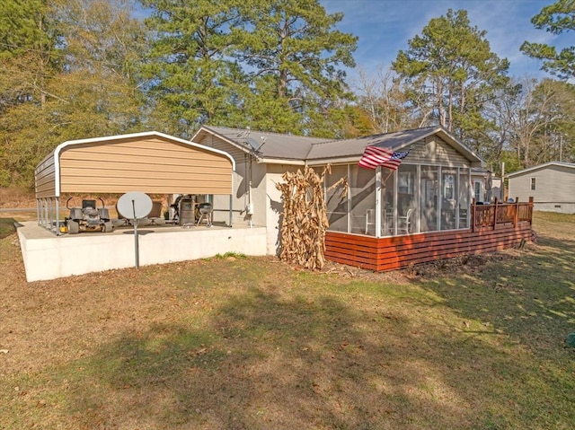 back of property with a carport, a yard, and a sunroom