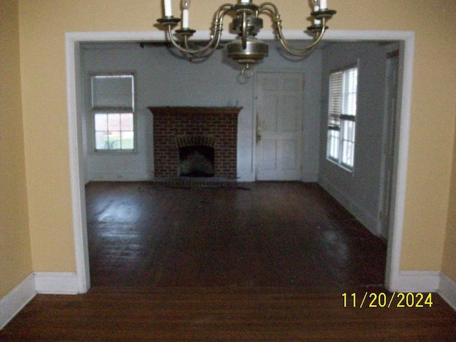 unfurnished living room featuring a chandelier and a brick fireplace