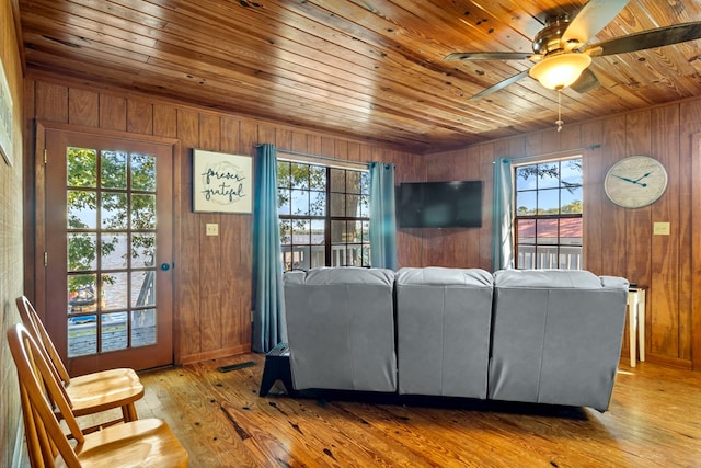 living room featuring light wood-type flooring, wood walls, wood ceiling, and ceiling fan