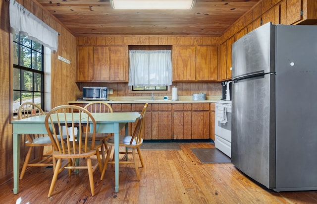 kitchen with wood ceiling, wooden walls, light hardwood / wood-style flooring, kitchen peninsula, and stainless steel appliances