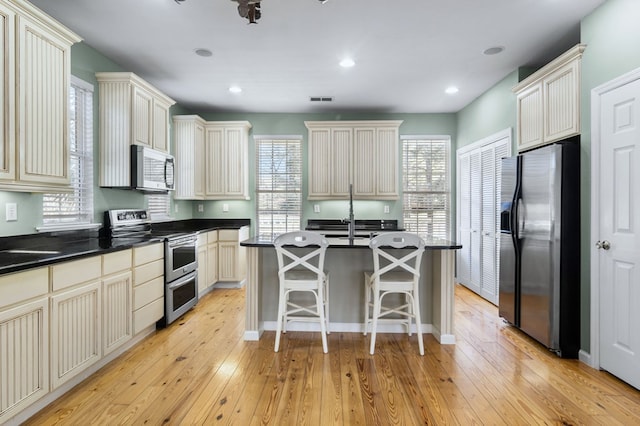 kitchen featuring a center island, stainless steel appliances, cream cabinetry, and light hardwood / wood-style flooring