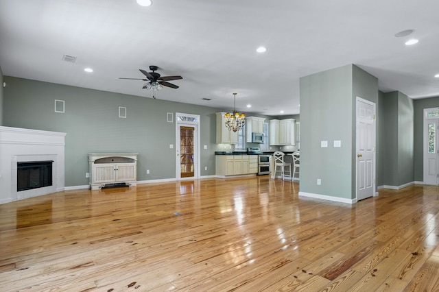 unfurnished living room with ceiling fan with notable chandelier and light hardwood / wood-style flooring