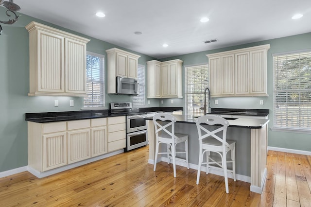 kitchen with light hardwood / wood-style floors, stainless steel appliances, cream cabinetry, and a kitchen island