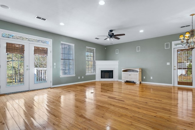 unfurnished living room with ceiling fan with notable chandelier, light hardwood / wood-style flooring, and french doors