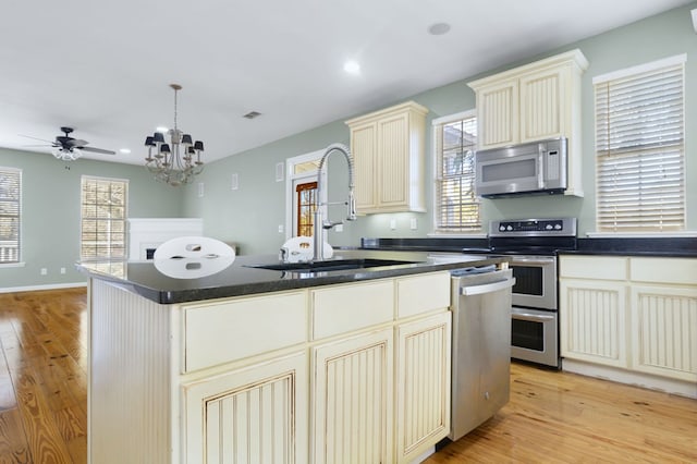 kitchen with hanging light fixtures, appliances with stainless steel finishes, sink, cream cabinetry, and a center island