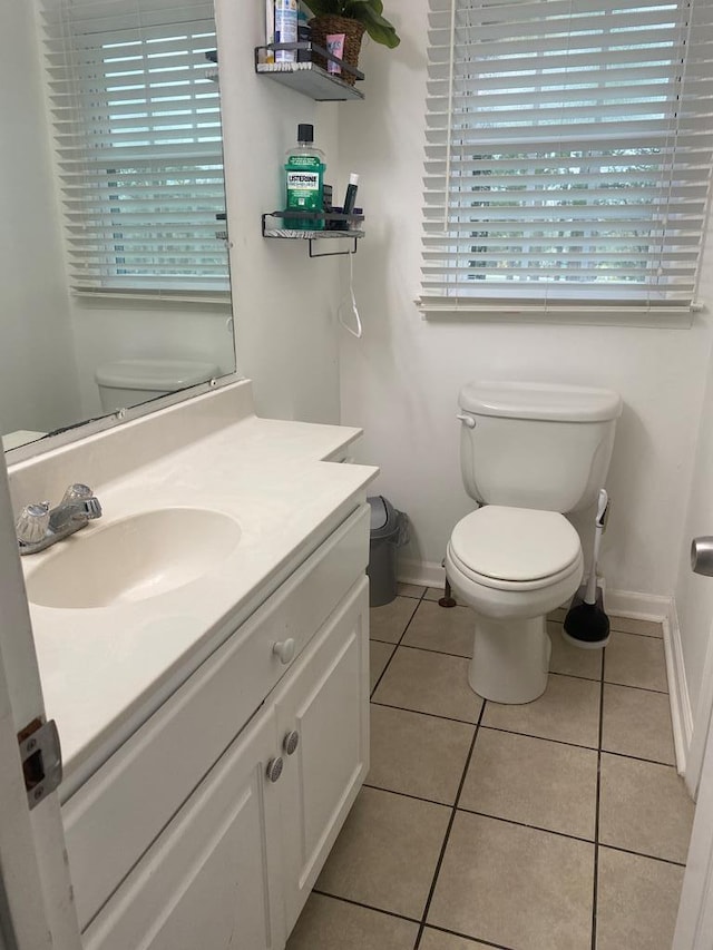 half bathroom with toilet, tile patterned floors, vanity, and baseboards