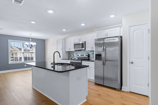 kitchen featuring white cabinetry, stainless steel appliances, an island with sink, sink, and hanging light fixtures