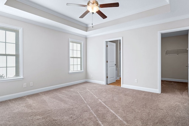 unfurnished bedroom with ceiling fan, light colored carpet, a tray ceiling, and a walk in closet