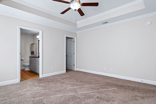 unfurnished bedroom with ceiling fan, connected bathroom, a tray ceiling, and ornamental molding