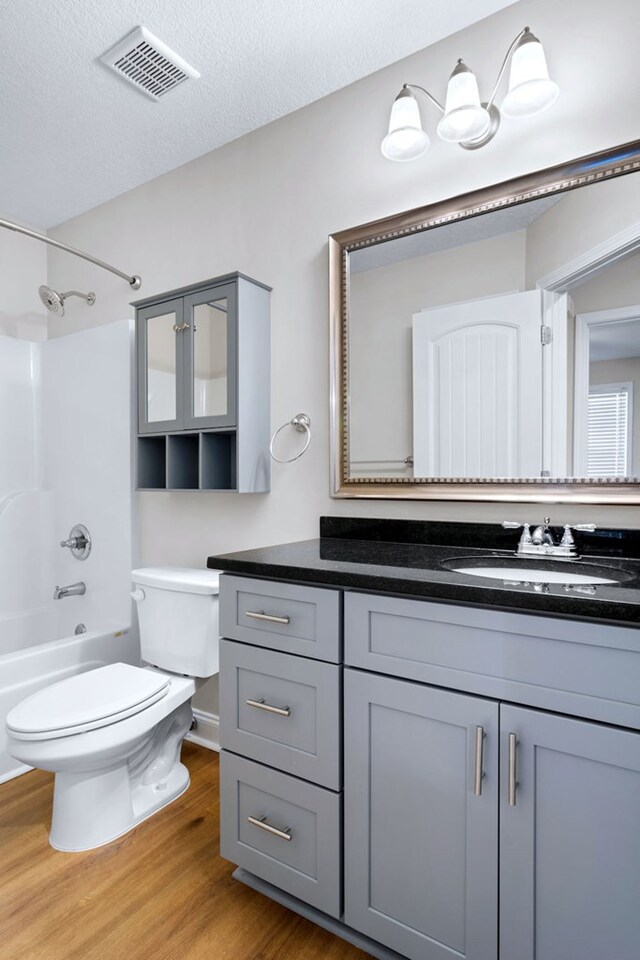 full bathroom with a textured ceiling, wood-type flooring, vanity, shower / bath combination, and toilet