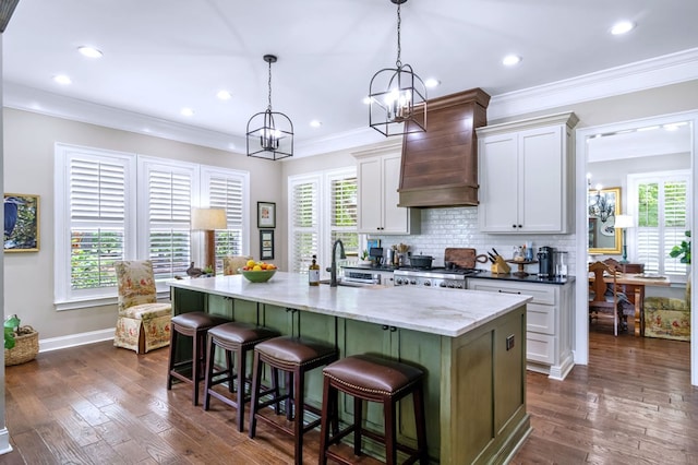 kitchen with white cabinetry, a kitchen breakfast bar, hanging light fixtures, a kitchen island with sink, and light stone countertops