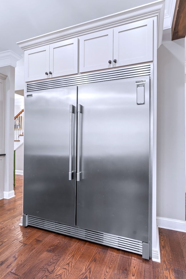 kitchen with ornamental molding, dark hardwood / wood-style floors, stainless steel built in fridge, and white cabinets