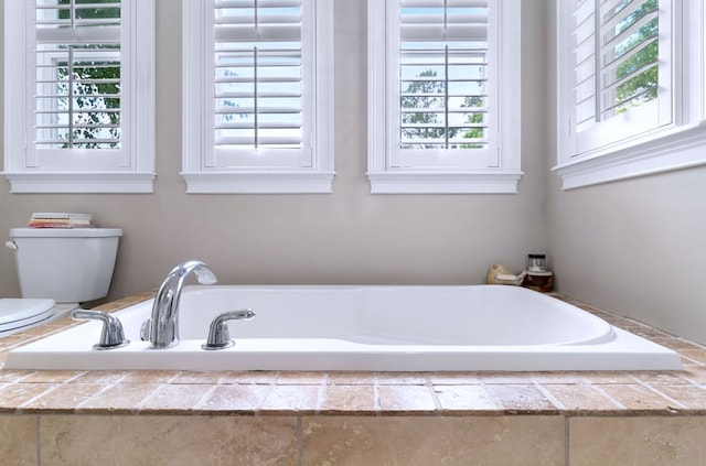 bathroom with a tub to relax in and toilet