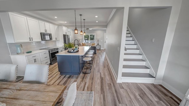 kitchen featuring a center island with sink, light wood-style floors, appliances with stainless steel finishes, white cabinets, and decorative backsplash