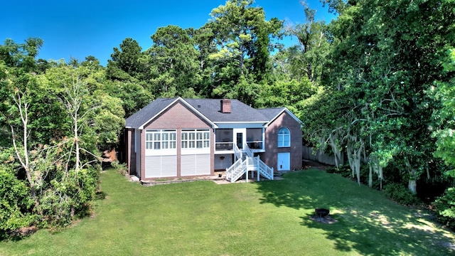 view of front facade with a sunroom, a chimney, stairs, a front lawn, and brick siding