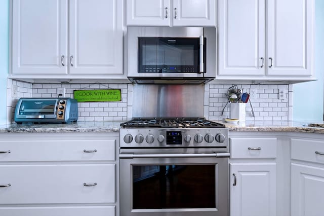 kitchen featuring stainless steel appliances, a toaster, white cabinetry, and light stone countertops