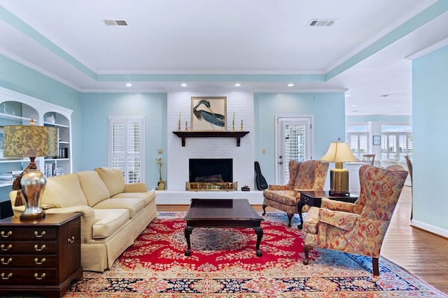 living area with a brick fireplace, crown molding, visible vents, and wood finished floors