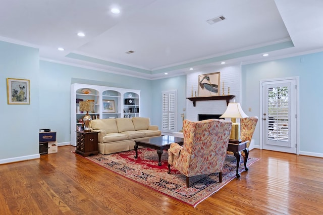 living area featuring a tray ceiling, visible vents, and wood finished floors