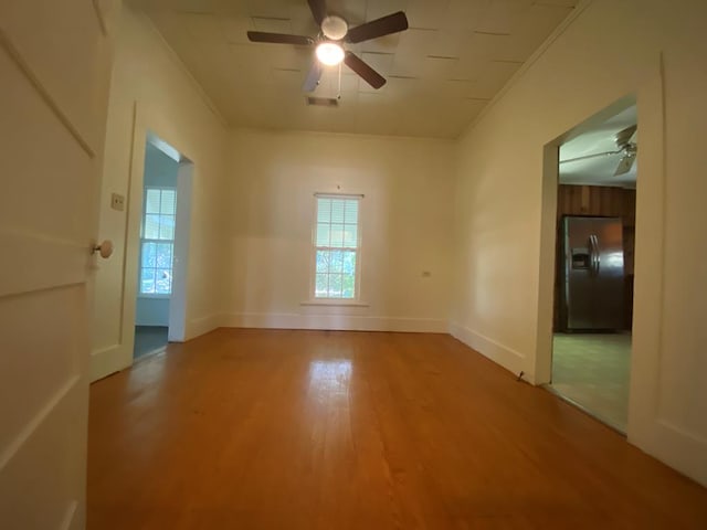 empty room featuring a wealth of natural light, wood-type flooring, ornamental molding, and ceiling fan