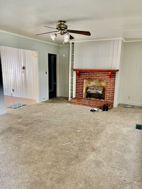 unfurnished living room featuring ceiling fan, a brick fireplace, ornamental molding, and carpet floors