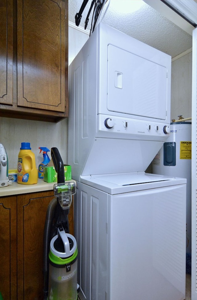 clothes washing area featuring a textured ceiling, stacked washer / dryer, and cabinets