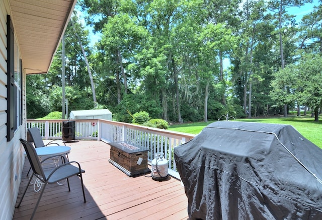 wooden terrace featuring a grill, a storage shed, a fire pit, and a lawn