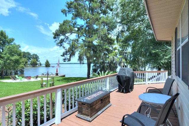 deck featuring a fire pit, a water view, grilling area, and a yard