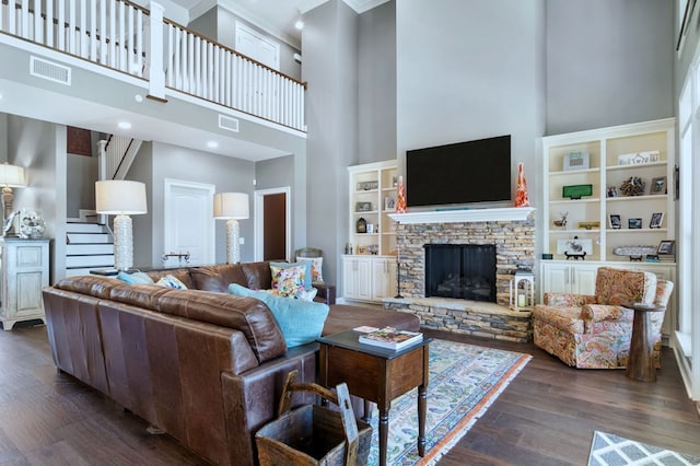 living room featuring dark wood-type flooring, stairway, visible vents, and a stone fireplace