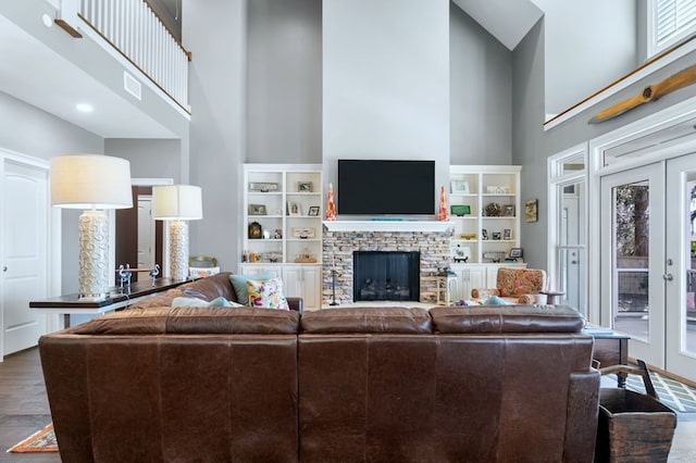 living area with a towering ceiling, a fireplace, wood finished floors, and french doors