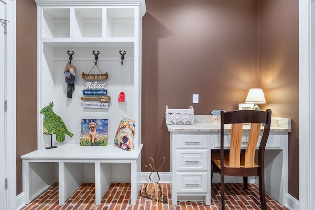 mudroom featuring brick floor, built in study area, and baseboards