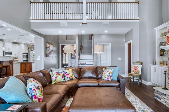 living area featuring dark wood-style flooring, visible vents, stairway, and a towering ceiling