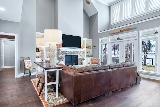 living room with dark wood-style flooring, french doors, a high ceiling, a stone fireplace, and baseboards