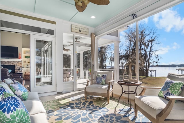 sunroom / solarium with a water view, ceiling fan, and a stone fireplace