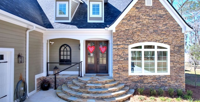 view of exterior entry featuring stone siding, french doors, and a shingled roof