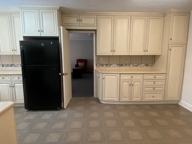 kitchen with black refrigerator, cream cabinetry, and tasteful backsplash