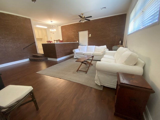 living room with ceiling fan with notable chandelier, brick wall, and dark hardwood / wood-style flooring