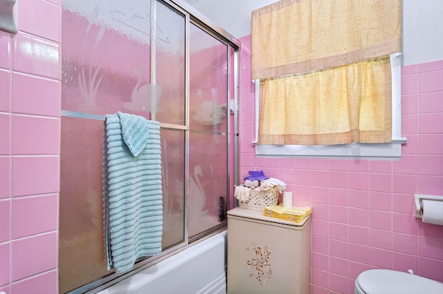 bathroom with enclosed tub / shower combo, toilet, and tile walls