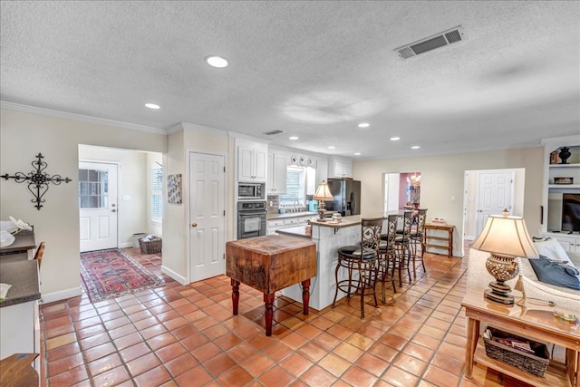 kitchen featuring white cabinets, a kitchen bar, light tile patterned floors, black appliances, and crown molding