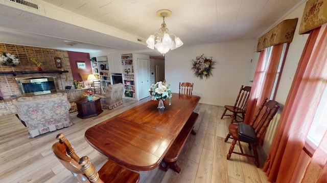 dining room with a chandelier, a brick fireplace, and light hardwood / wood-style floors