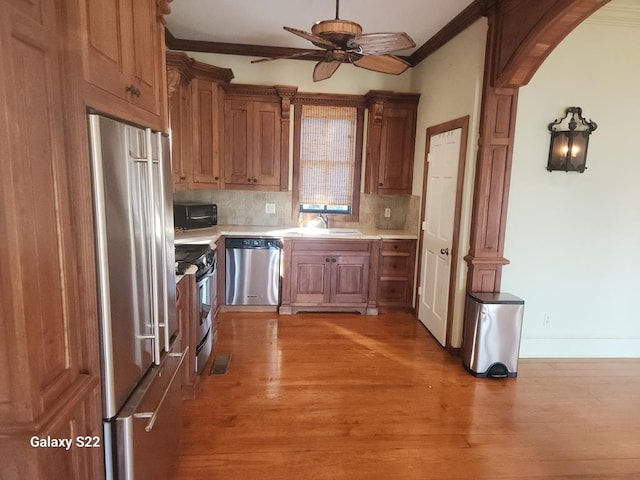 kitchen with appliances with stainless steel finishes, wood-type flooring, sink, backsplash, and ornamental molding