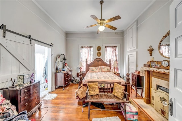 bedroom featuring ceiling fan, a barn door, light hardwood / wood-style flooring, and crown molding