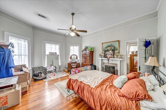 bedroom with ceiling fan, crown molding, light hardwood / wood-style floors, and a textured ceiling