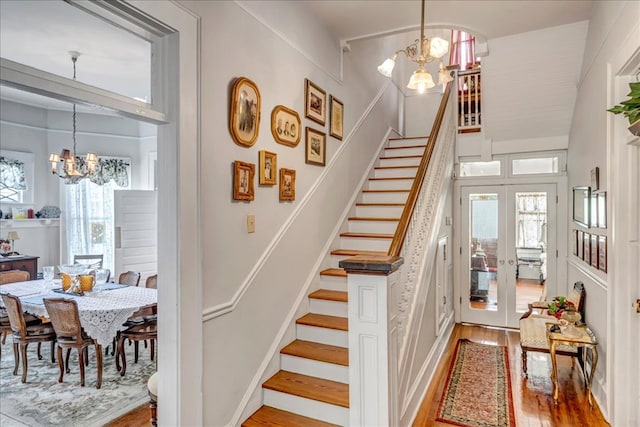 staircase with french doors, wood-type flooring, and a notable chandelier