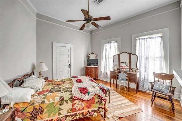 bedroom with ceiling fan, hardwood / wood-style floors, a textured ceiling, and crown molding