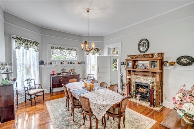 dining room with a stone fireplace, light hardwood / wood-style flooring, ornamental molding, and a notable chandelier